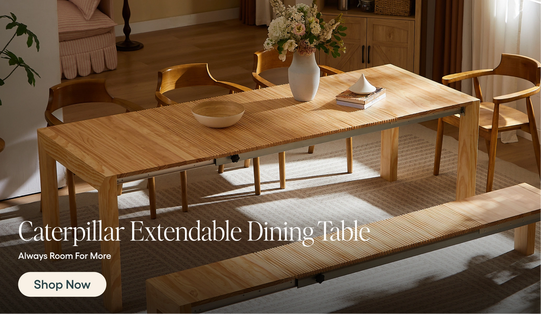 A light natural wood caterpillar extendable dining table shown in a warm, modern dining room setting with matching wooden chairs and a bench. White text overlay at the bottom reads 'Caterpillar Extendable Dining Table' with a 'Shop Now' button.