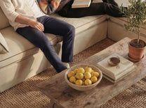 Person sitting on a beige sofa with a wooden coffee table featuring a bowl of lemons.