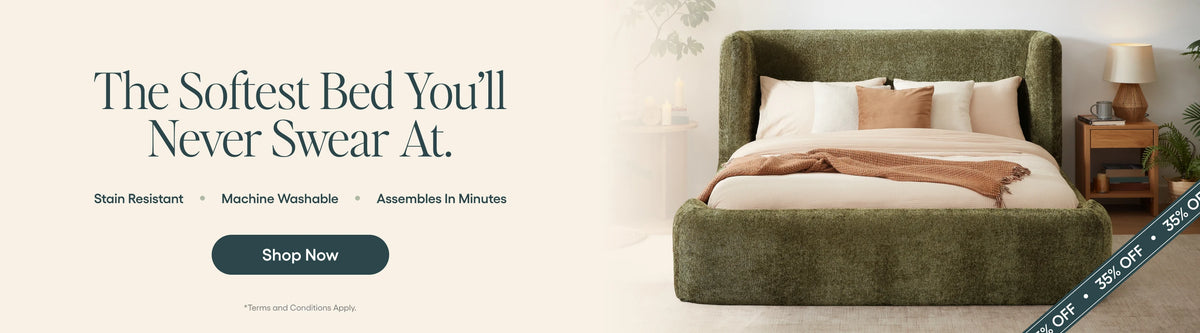 An upholstered bed with a tall rounded headboard and footboard in a muted olive green fabric, styled with white and tan pillows and a beige throw blanket. Large marketing text on the left reads, 'The Softest Bed You'll Never Swear At.