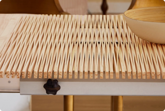 Close-up of a light natural wood slatted tabletop or drawer surface with a dark knob on the front and a matching wood bowl partially visible in the upper right.