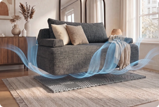 A modern gray fabric sofa with two beige throw pillows and a cream throw blanket, set in a bright living room with blue airflow graphics indicating cooling. The sofa sits on a gray patterned rug over a light wood floor.