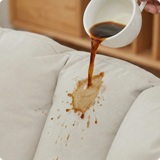 Coffee being poured from a white cup onto a beige fabric surface, causing a stain.
