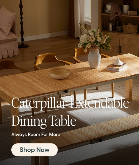 A Caterpillar extendable dining table in a warm wood finish, styled in a cozy dining room setting with chairs, a vase of flowers, and a bowl. The image includes text overlays reading 'Caterpillar Extendable Dining Table', 'Always Room For More', and a 'Shop Now' button.